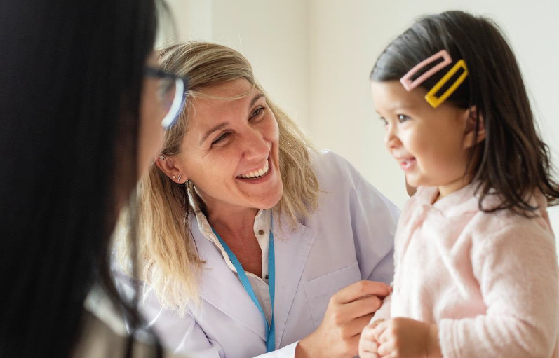 A physician smiles at a small child as the parent looks on